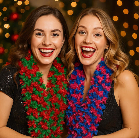 Two women smiling widely wearing colorful feather boas in front of a festive background.