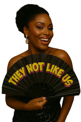 Woman holding a colorful "They Not Like Us" Folding Fan for Photo Booth Party, adding fun to events.