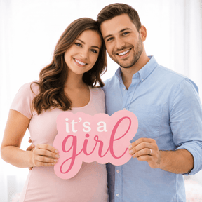 Smiling couple holding a sign saying it's a girl! as part of a fun prop for baby announcements.